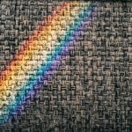 A rainbow light casts vibrant colors on a textured woven fabric surface, creating a unique pattern.