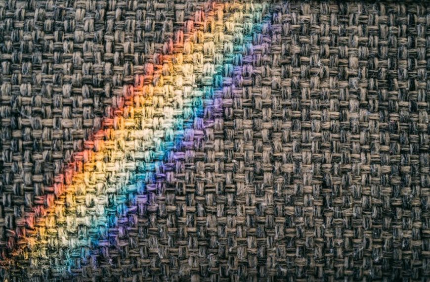 A rainbow light casts vibrant colors on a textured woven fabric surface, creating a unique pattern.