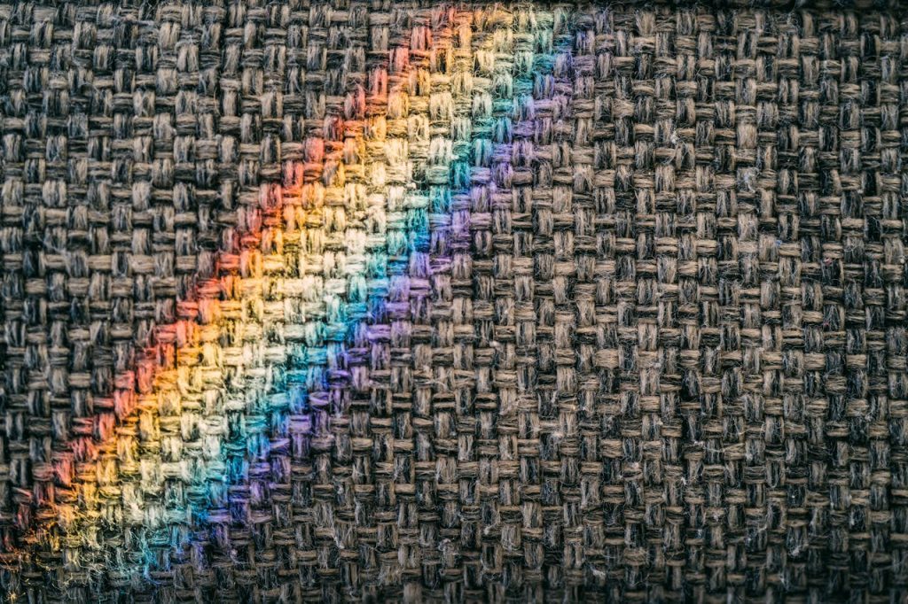 A rainbow light casts vibrant colors on a textured woven fabric surface, creating a unique pattern.