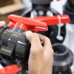 Close-up of hands examining a Hydroplast industrial valve at a trade expo.